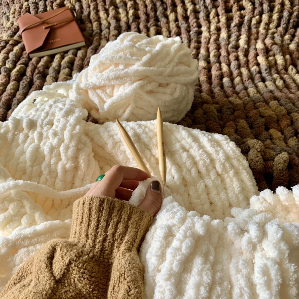 Hand on knitting needle working on white blanket