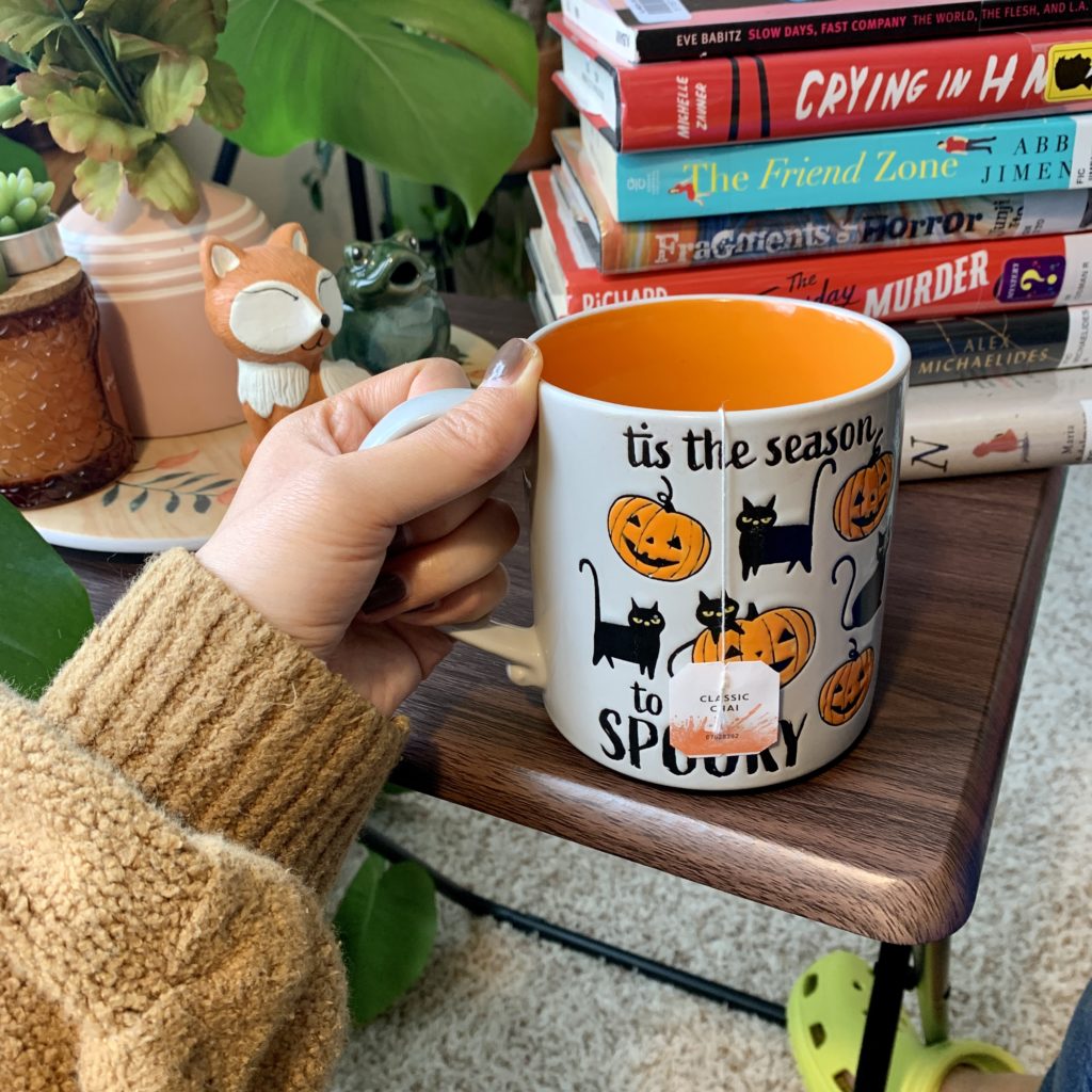 Hand holding 'Tis the Season to Be Spooky mug with tea bag