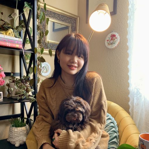 Woman holding brown dog next to plant shelf