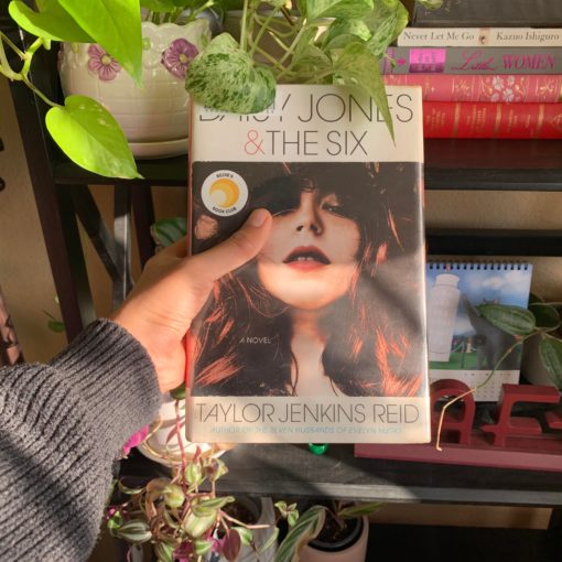 Hand holding copy of Daisy Jones and The Six next to plants